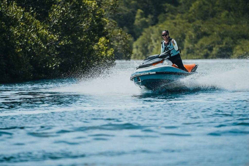 Iate de luxo branco navegando em mar verde-esmeralda, acompanhado por dois jet skis deixando rastros de espuma.
