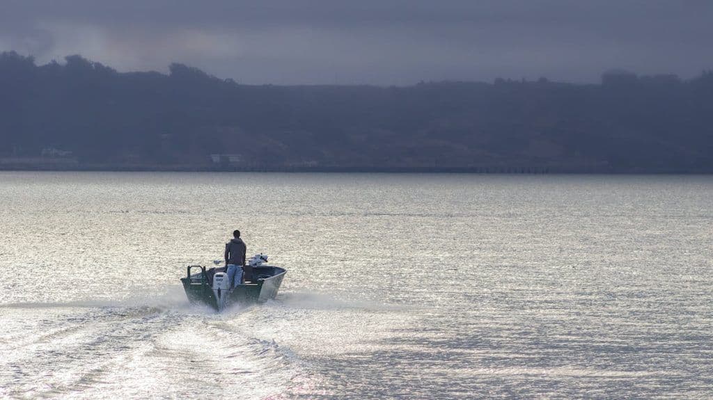 Porto com diversos barcos e embarcações atracados, com montanhas ao fundo sob céu claro