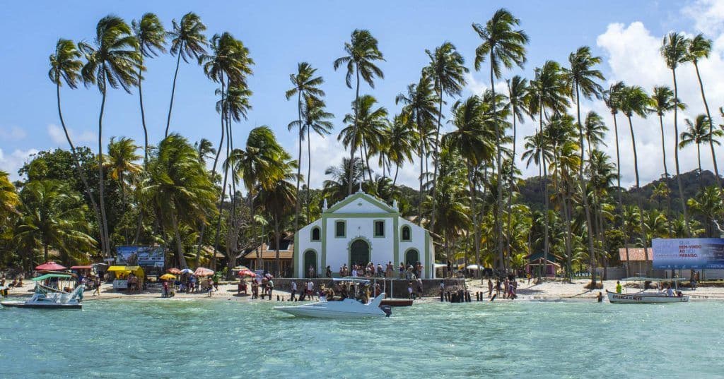 Igreja de São Benedito à beira-mar na Praia dos Carneiros (PE), cercada por coqueiros altos e águas calmas